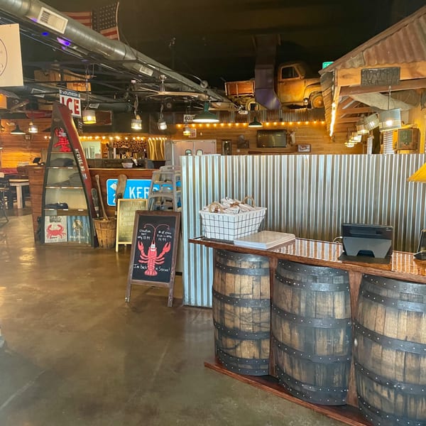 Captain John's seafood restaurant interior with rustic decor, a lobster chalkboard, and barrel-themed counter.