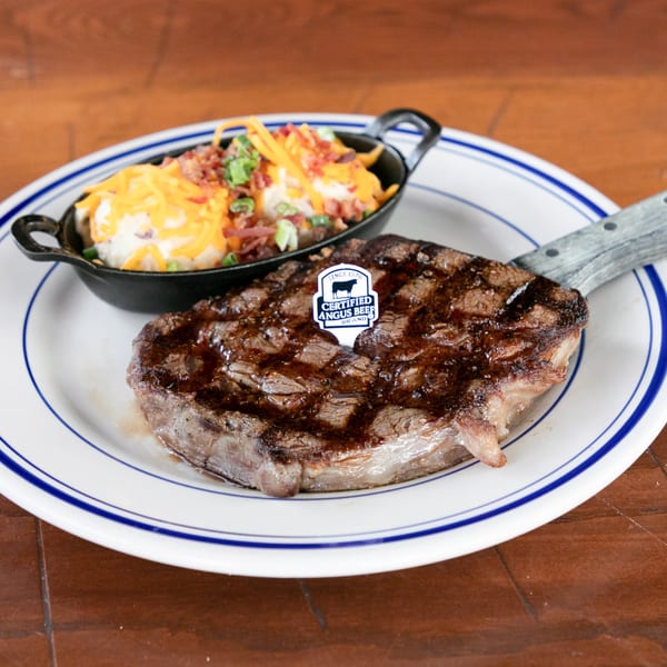 Grilled steak with a Certified Angus Beef pick, served with loaded mashed potatoes in a cast iron dish.