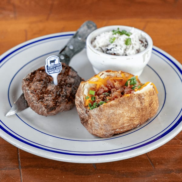 Captain John's steak dinner with a baked potato and a side of rice on a white plate.