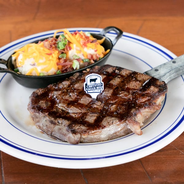 Grilled steak with a Certified Angus Beef pick, served with loaded mashed potatoes in a cast iron dish.