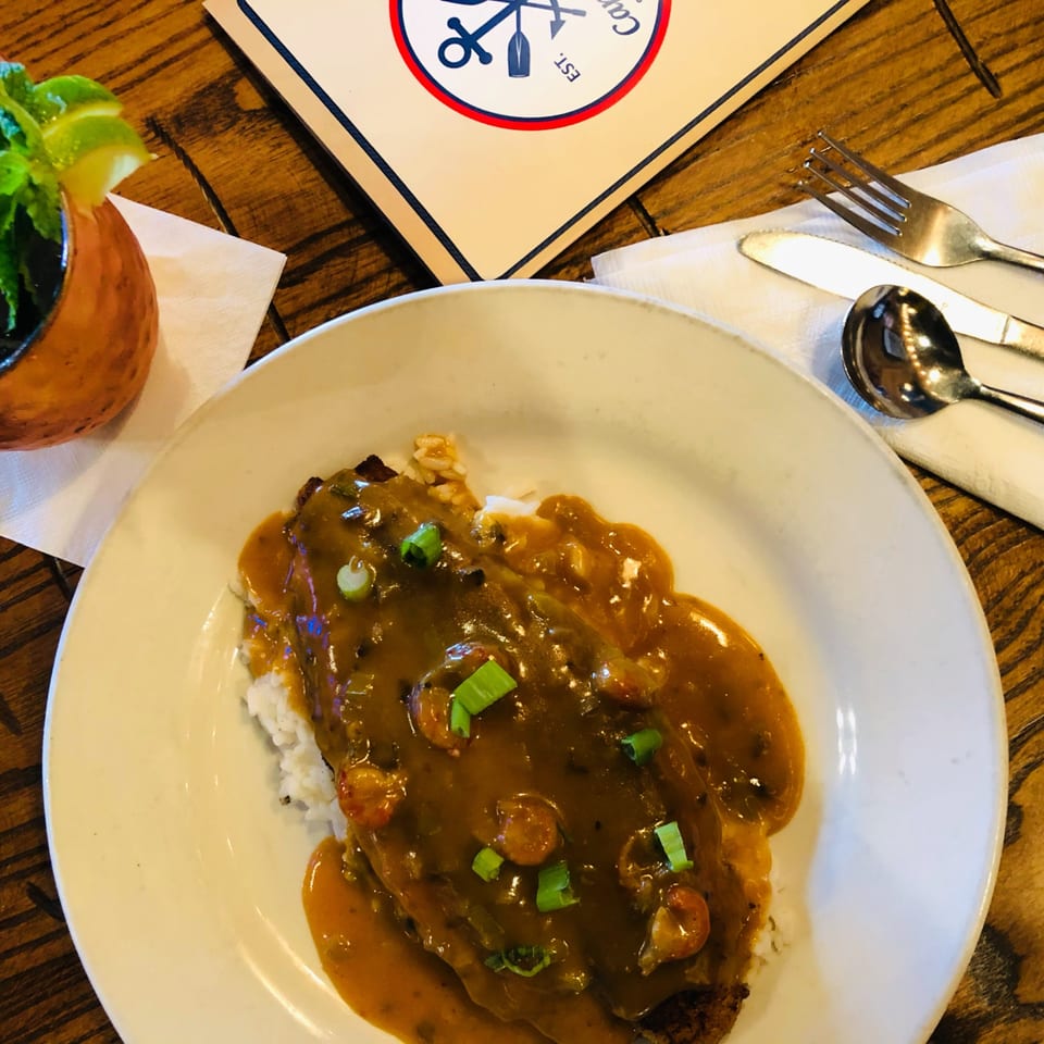 Captain John's seafood dish with shrimp and gravy over rice, a drink, and silverware.