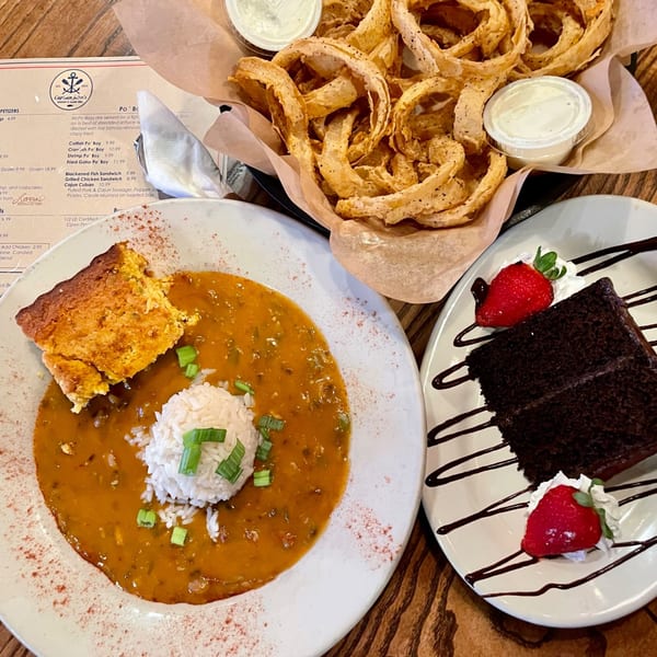Captain John's seafood gumbo with rice and cornbread, a basket of onion rings, and chocolate cake.