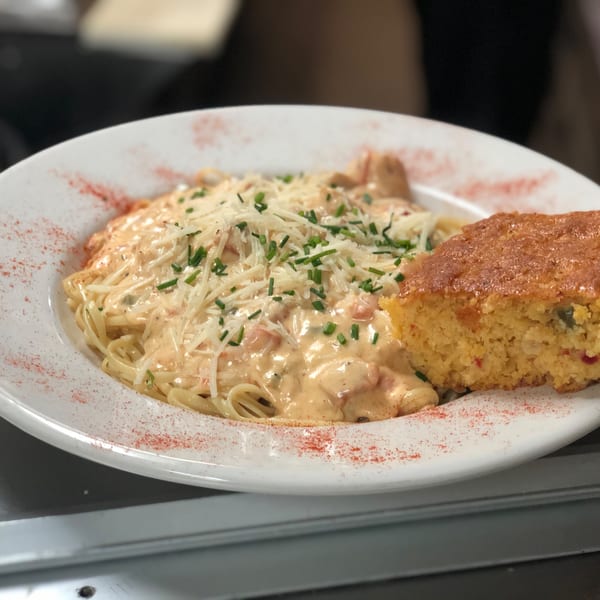 Captain John's creamy seafood pasta with shredded cheese and chives, served with a side of cornbread.