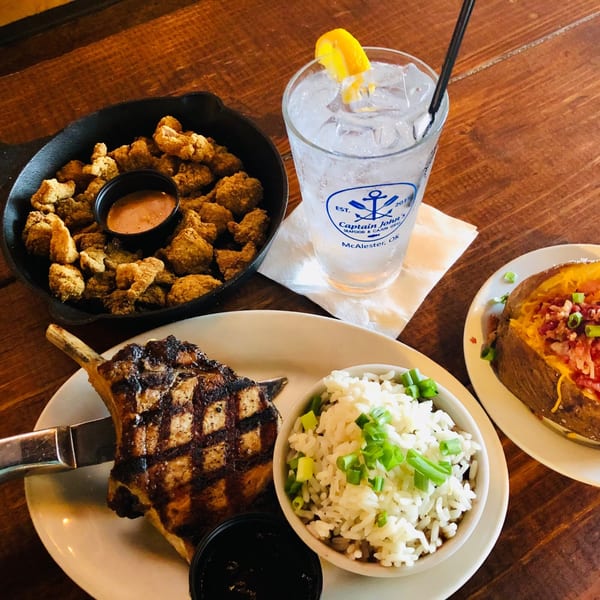 Captain John's seafood meal with fried oysters, grilled pork chop, rice, and a loaded baked potato.