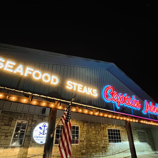 Captain John's seafood restaurant exterior at night, with bright neon and bulb signs, and an American flag.