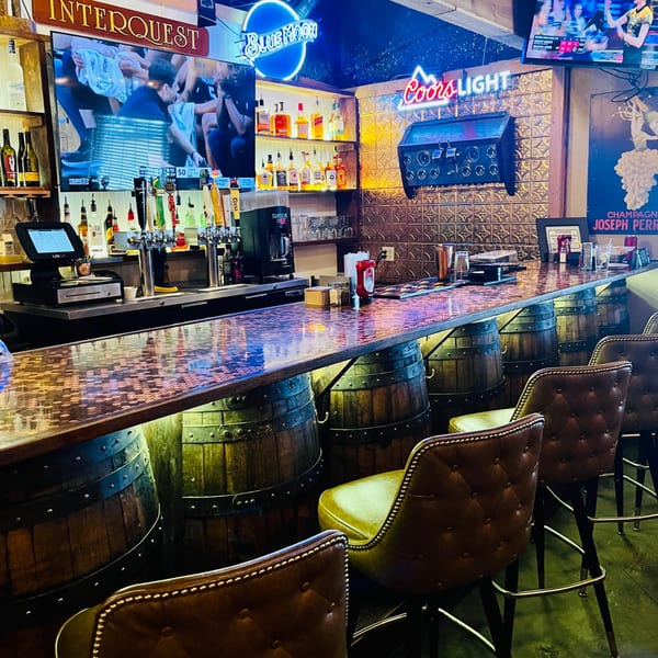 Captain John's bar with barrel-themed seating, neon signs, and a TV showing sports.