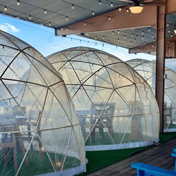 Outdoor dining igloos with tables and chairs under a string-lit canopy at Captain John's.