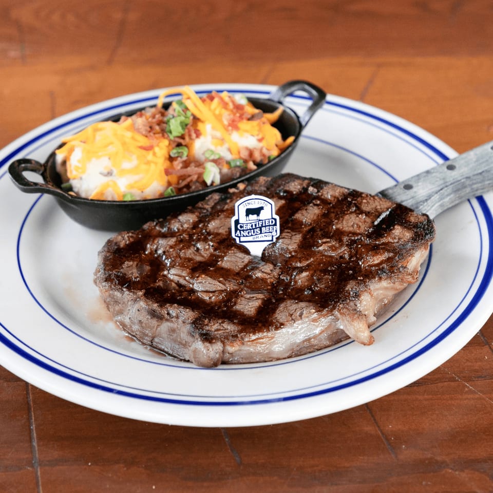 Grilled steak with a Certified Angus Beef pick, served with loaded mashed potatoes in a cast iron dish.
