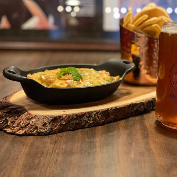 Captain John's seafood dip in a black skillet with tortilla chips and a beer.