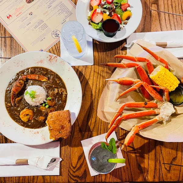 Captain John's seafood feast with gumbo, crab legs, corn, salad, and drinks on a wooden table.