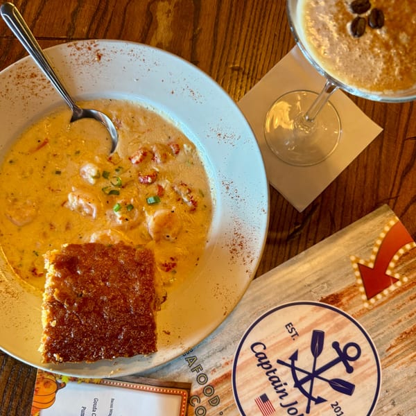 Captain John's seafood bisque with cornbread and a coffee martini on a wooden table.