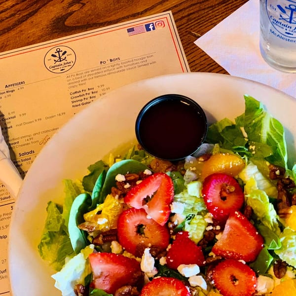 A fresh salad with strawberries, pecans, and feta cheese, next to a Captain John's menu.