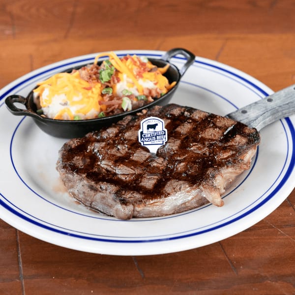 Grilled steak with a Certified Angus Beef pick, served with loaded mashed potatoes in a cast iron dish.