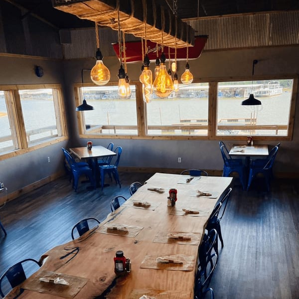 Captain John's dining room with a long wooden table, blue chairs, and water views.