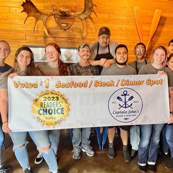 Captain John's staff holding a banner celebrating their "Voted #1 Seafood / Steak / Dinner Spot" award.
