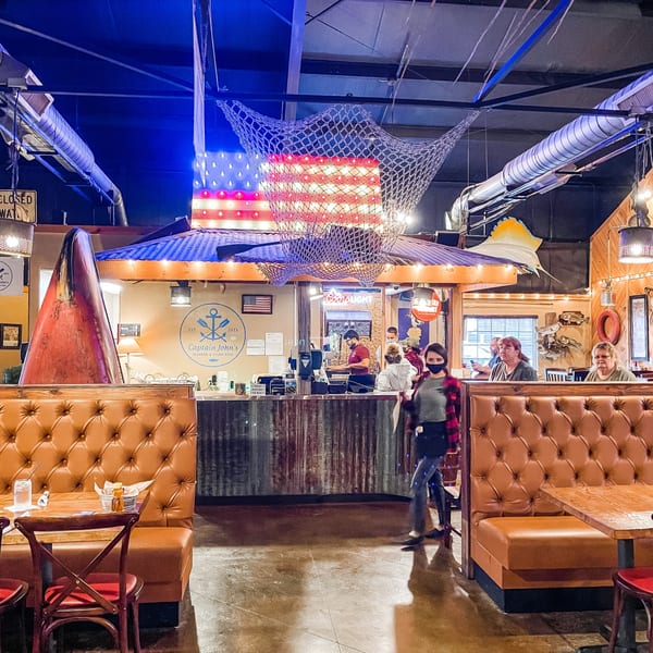 Captain John's seafood restaurant interior with booths, a bar, and nautical decor including a lighted American flag.