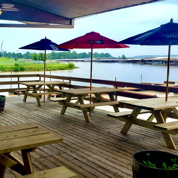 Outdoor dining deck at Captain John's with picnic tables, umbrellas, and a view of the lake.