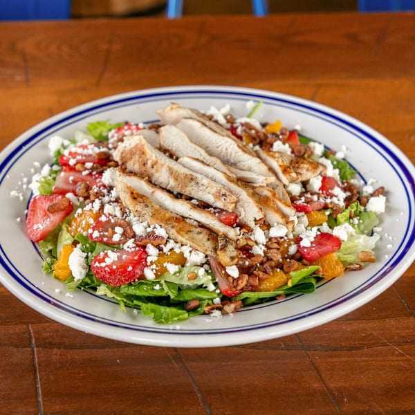 Grilled chicken salad with strawberries, oranges, pecans, and feta cheese on a white plate.